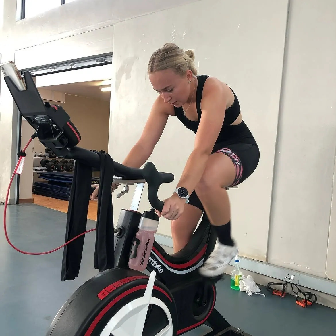 Athlete pushing hard on a Wattbike in the lab, with a water bottle in the cage