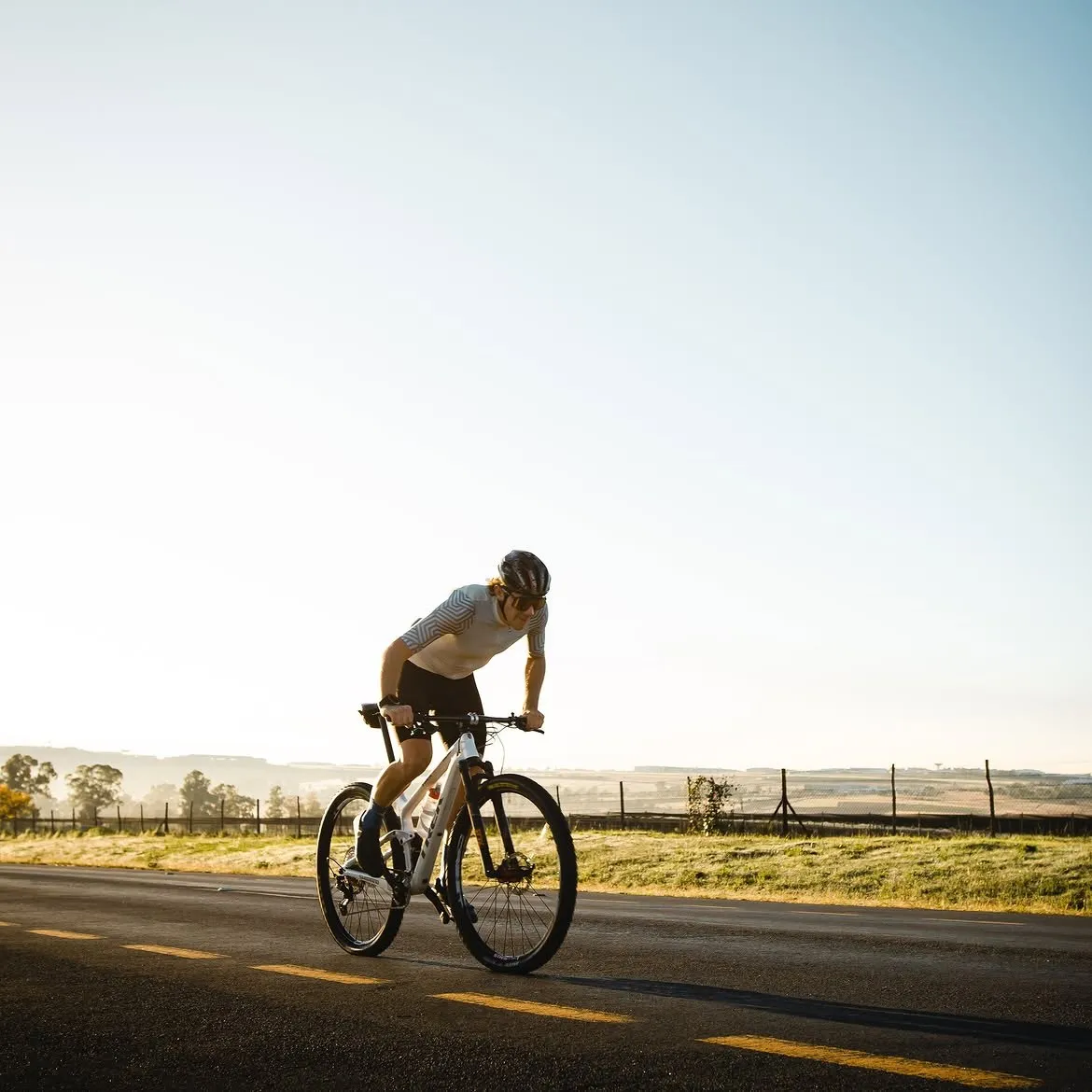 Cyclist riding an open country road at sunrise