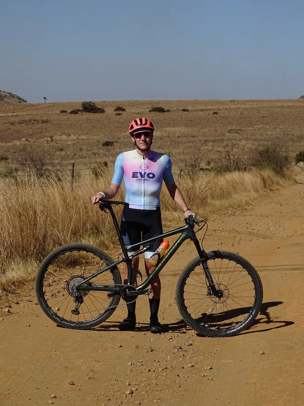 Mountain biker in EVO kit standing with their bike on a dry gravel road