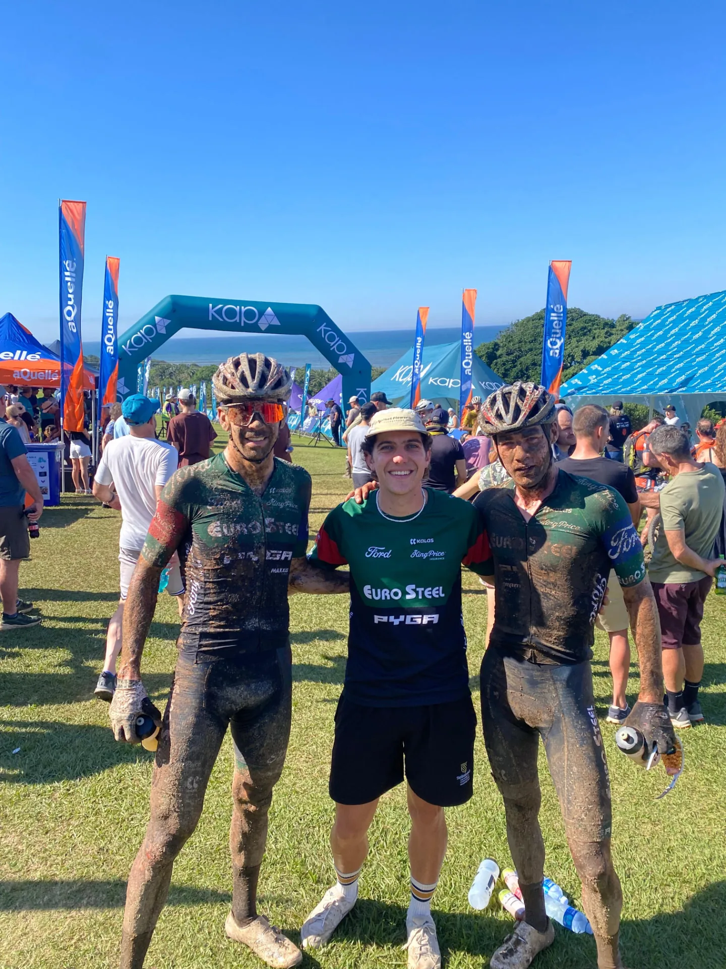 Two mud-covered mountain-bike racers with an EVO team member at the race finish