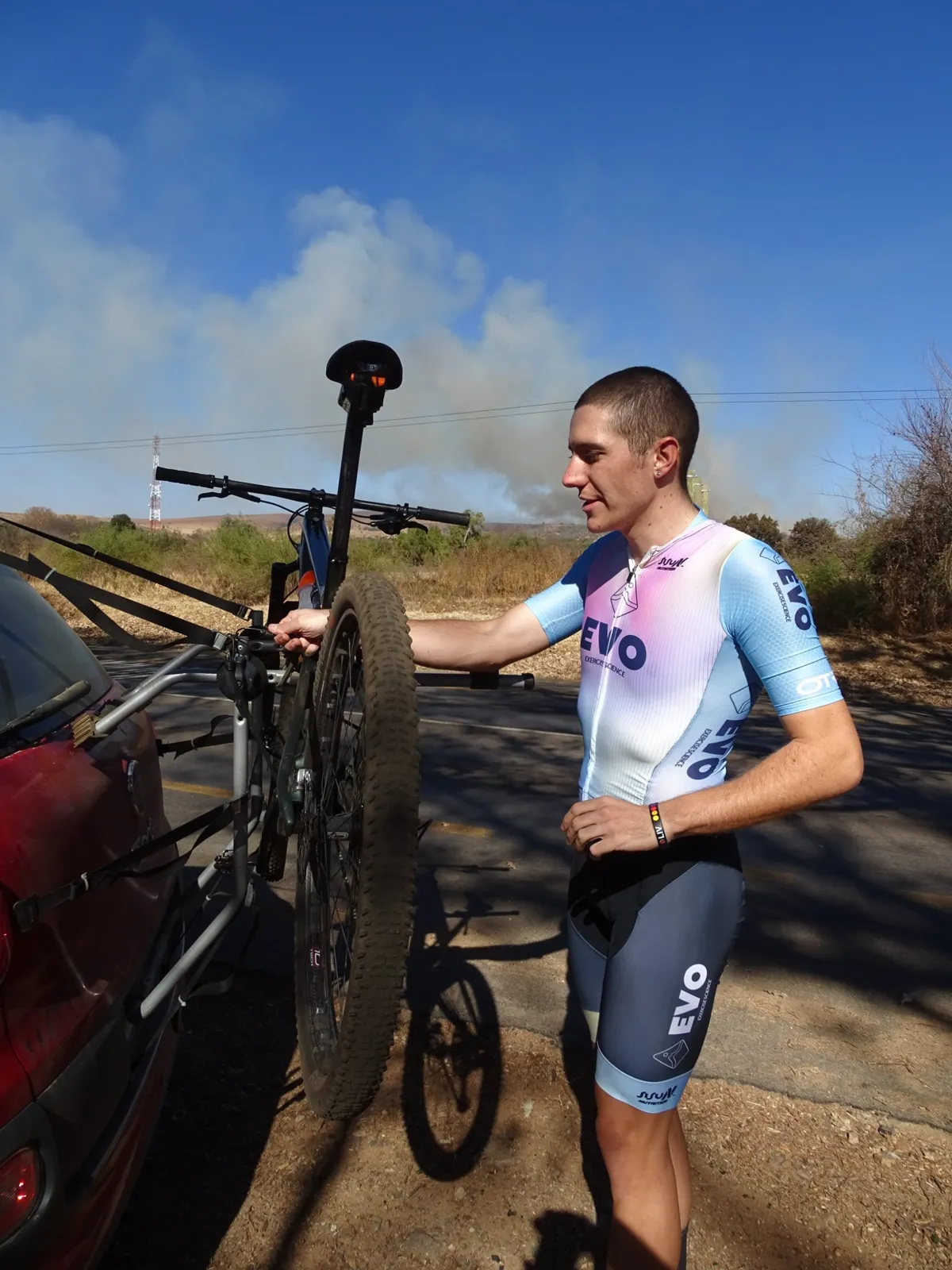 Rider in EVO kit loading a mountain bike onto a car rack