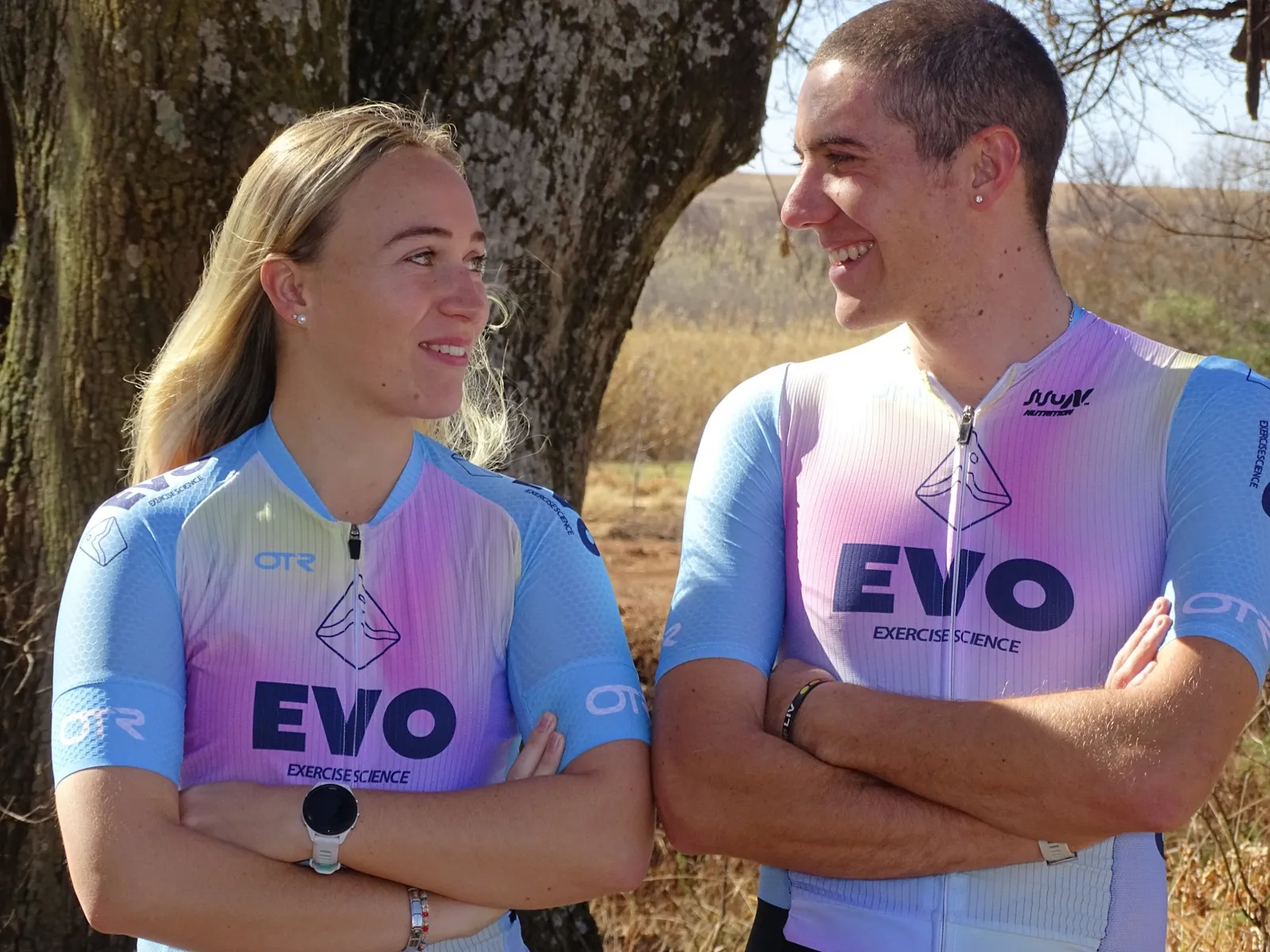 Two athletes in EVO kit smiling at each other under a tree