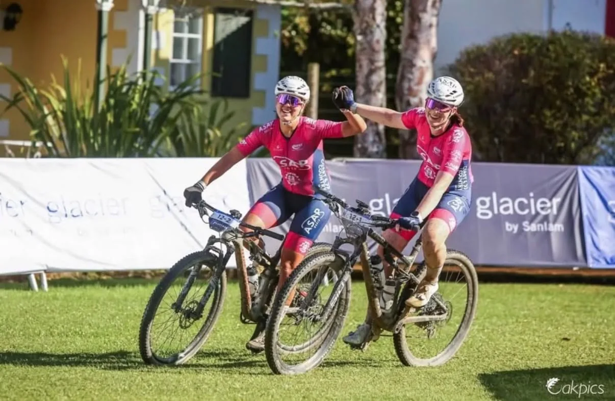 Two mountain-bike teammates in pink kit celebrating together at a stage-race finish